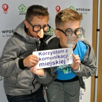 Dwóch chłopców w przebraniu prezentuje napis: Korzystam z komunikacji miejskiej